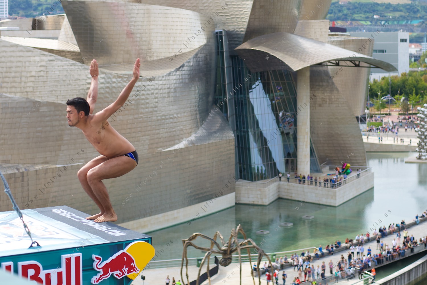 Gesto del clavadista antes del comienzo del salto en en el Red Bull Cliff Diving en Bilbao con el Guggenheim al fondo