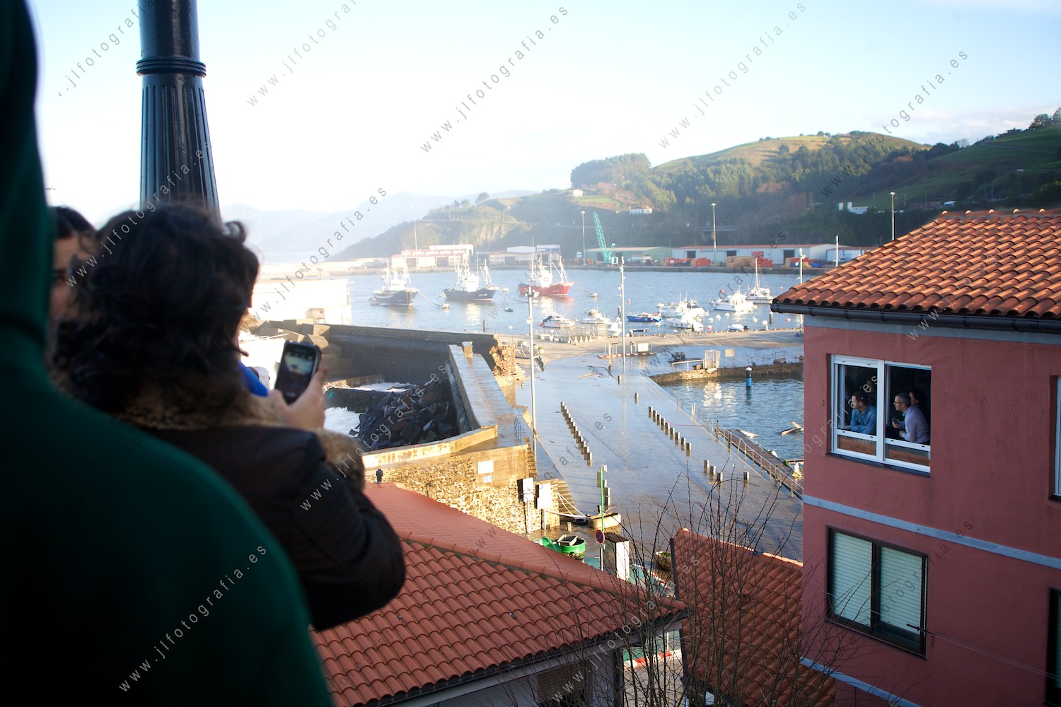 Los vecinos de Bermeo miran hacia el mar viendo llegar las olas gigantes que revientan los diques del puerto