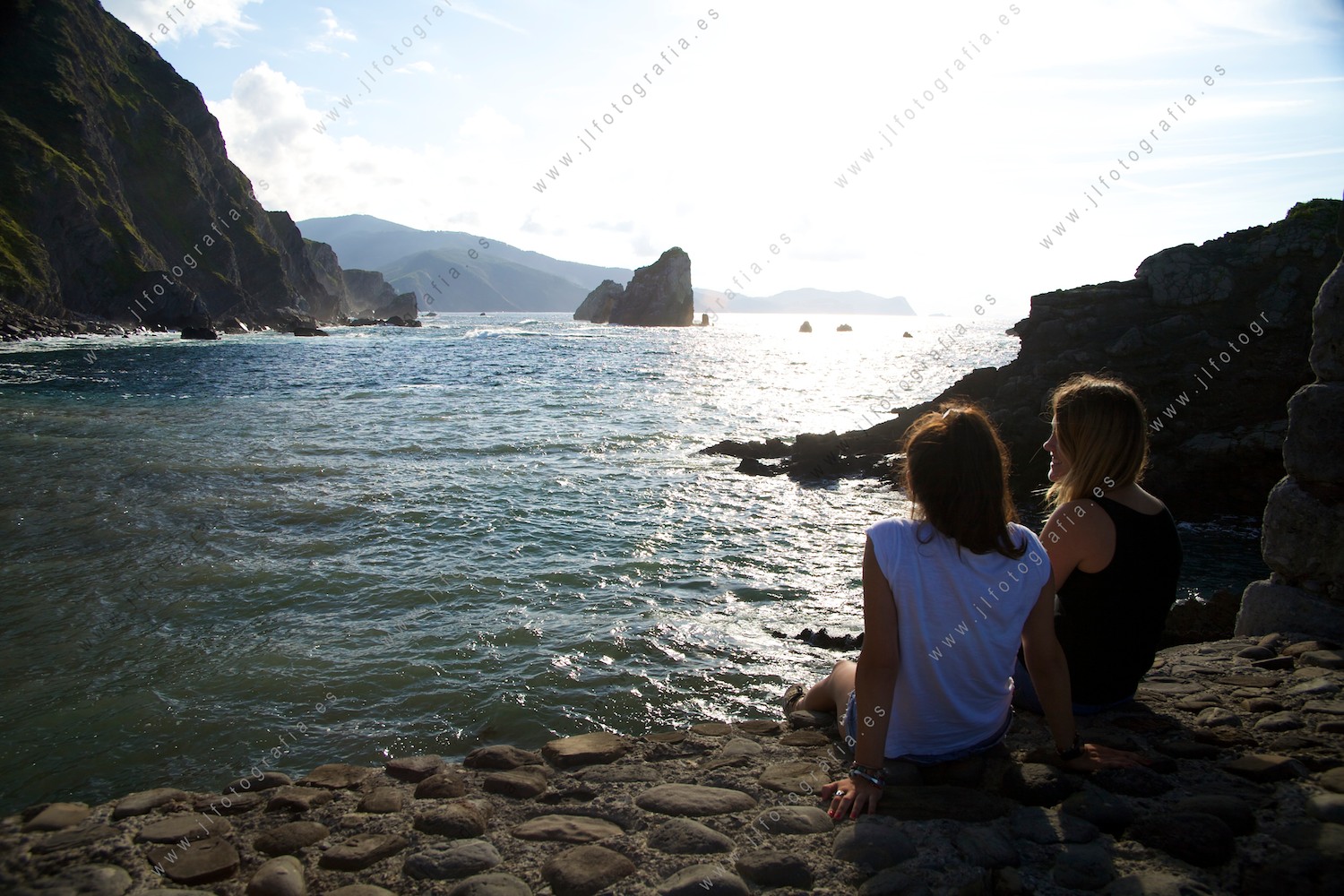 Dos jóvenes mujeres miran hacia la catedral de la costa de Bakio, al atardecer