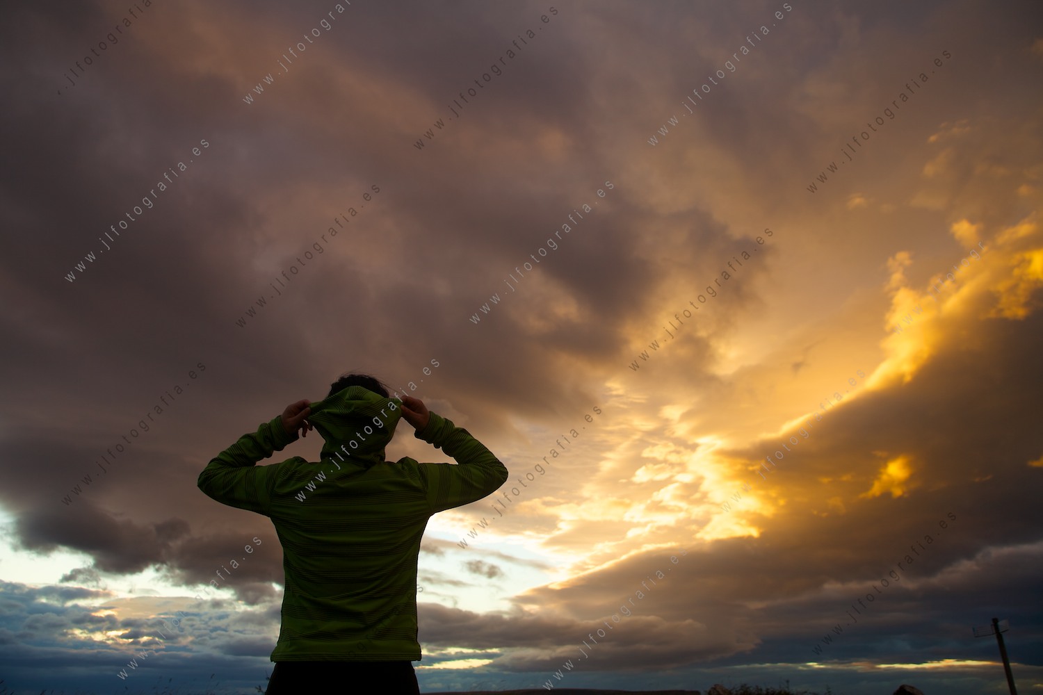 Joven poniendose el gorro para resguardarse del fuerte viento en el desfiladero del salto del Nervión en Délika con una puesta impresionante