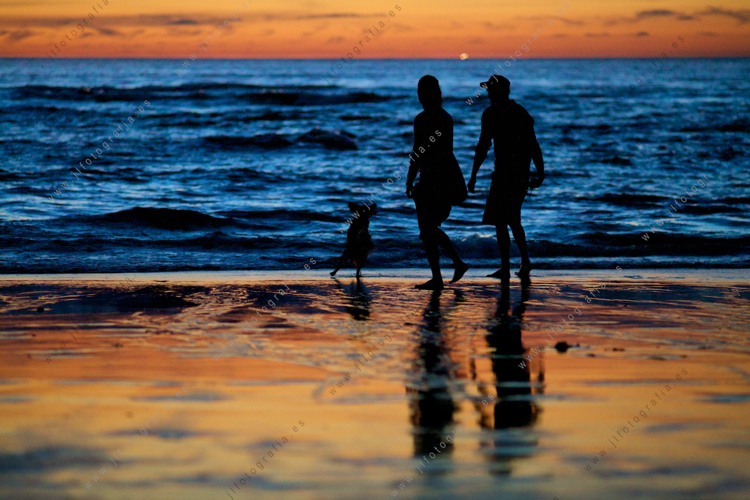 Una pareja disfruta del fin del día con los colores intensos del mar y el cielo.
